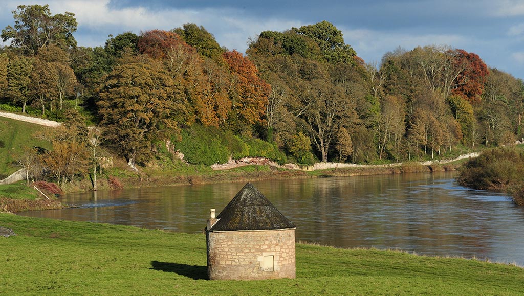 Milne Graden fishing sheil on the river tweed overlooked by a blase of autumn trees